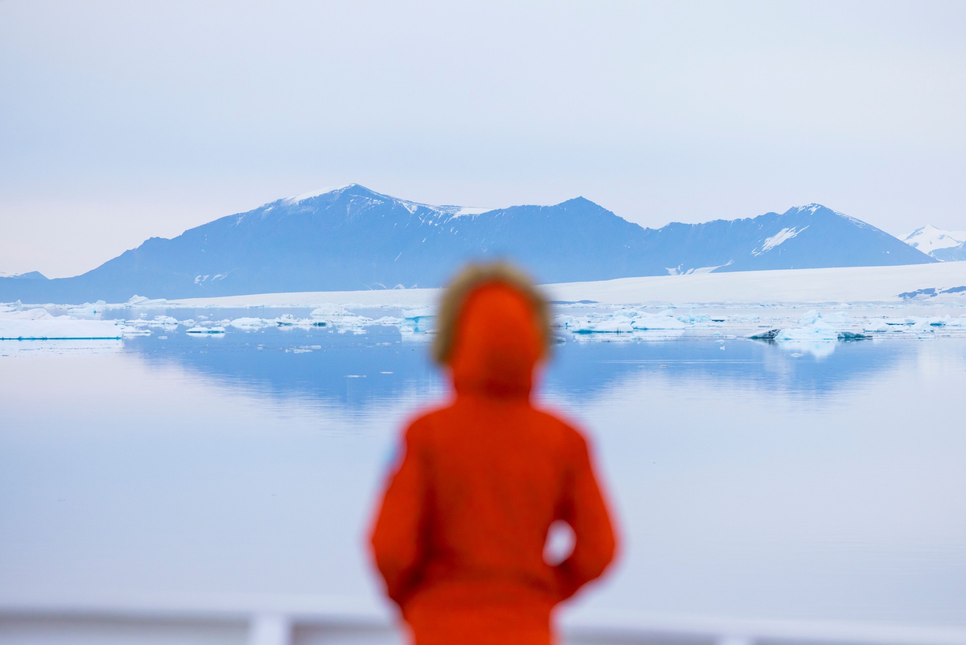 Woman in a red jacket standing on the bow of a ship in Antarctica—embracing the spirit of adventure through a personalized polar cruise experience with Curated Passports.
