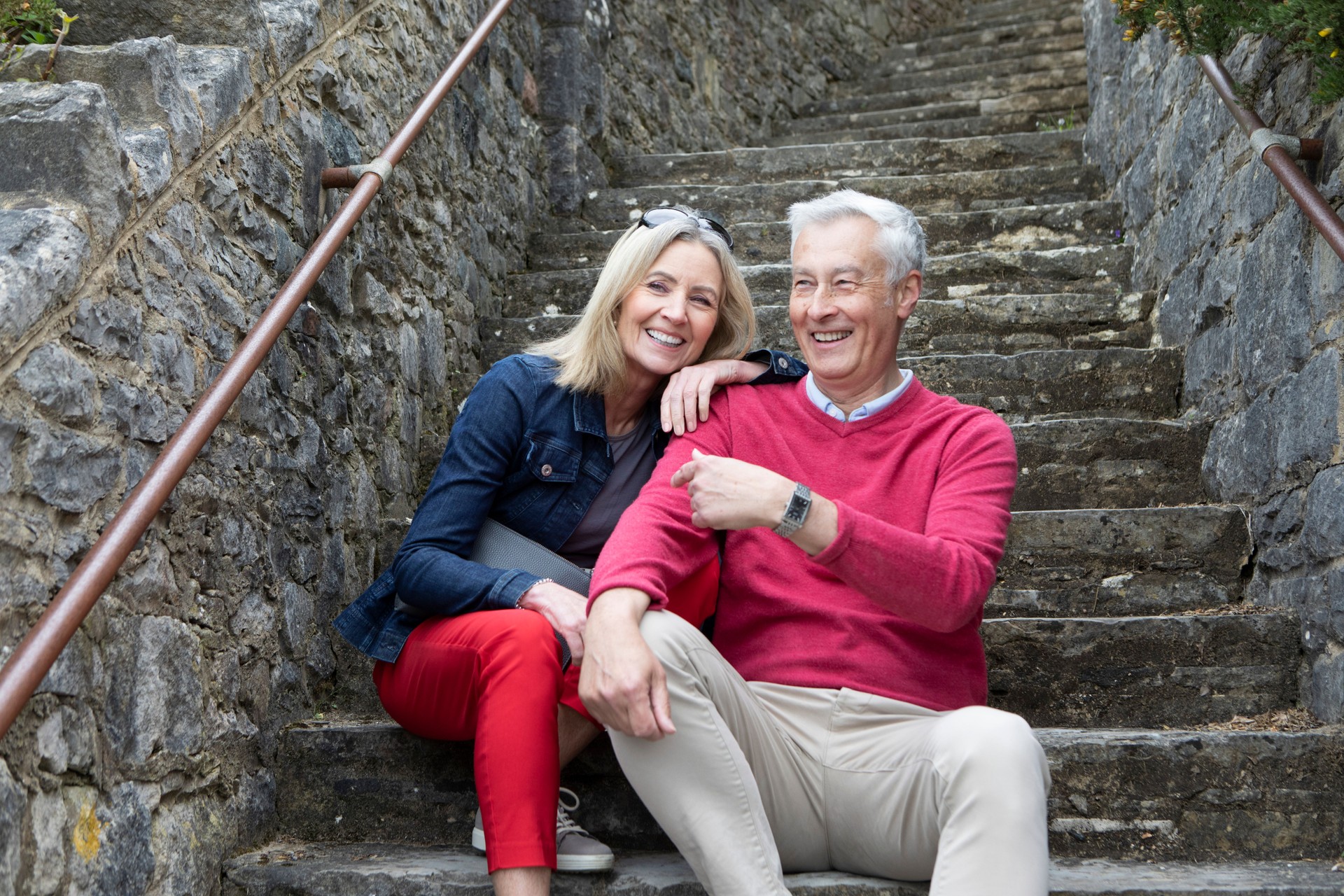 Cheerful mature couple sitting on seaside stone steps during a curated vacation planned by Curated Passports