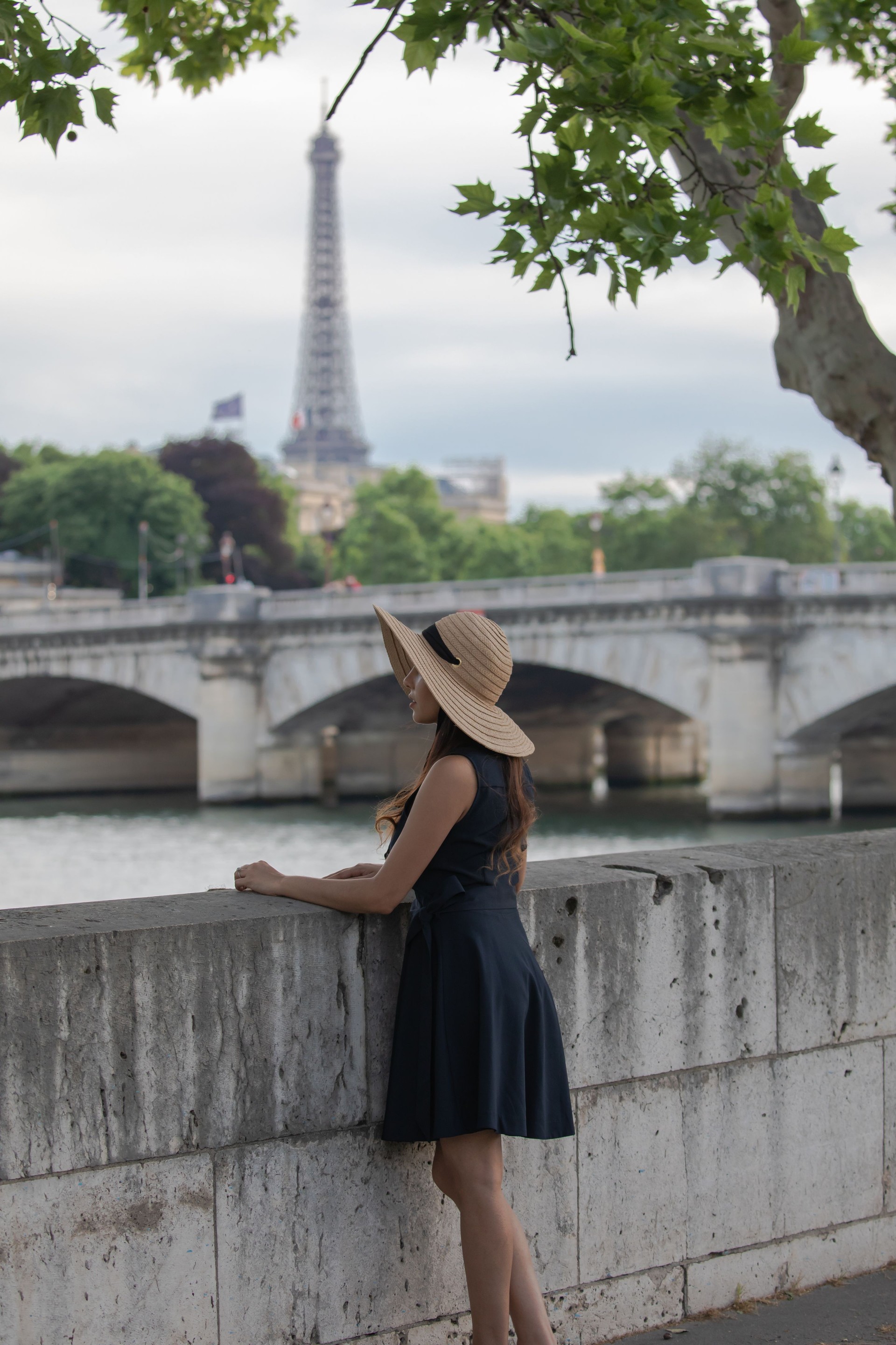 Stylish woman in a blue dress and hat gazing at the Seine River and Eiffel Tower in Paris—capturing the elegance, freedom, and personal connection at the heart of Curated Passports’ custom travel experiences.